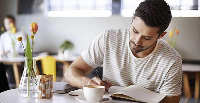 Uomo che scrive il proprio diario seduto in un bar